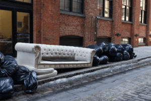 Un divano bianco di gradi dimensioni lasciato sul bordo della strada insieme a dei sacchi neri
