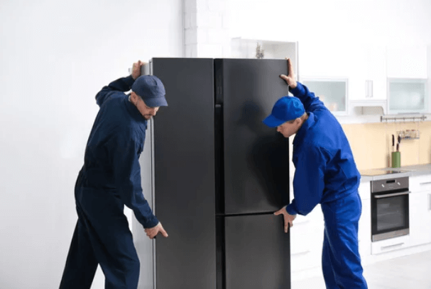 Due addetti intenti nello spostamento di un frigorifero con congelatore