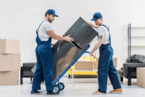 Due traslocatori, che indossano una salopette da lavoro blu, mentre spostano su un carrello un frigorifero nuovo