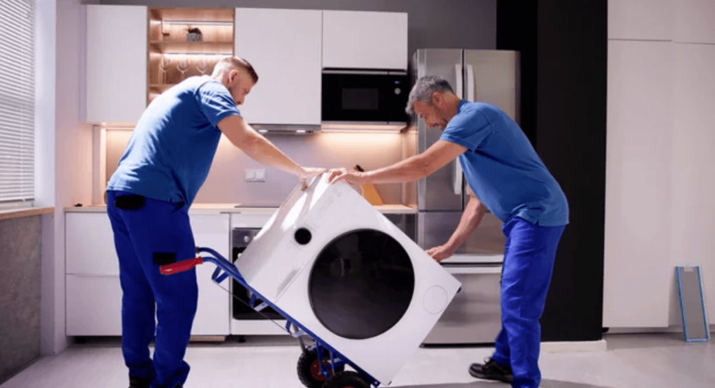 Due traslocatori, con le divise di colore blu, mentre caricano una lavatrice su di un carrello per trasloco