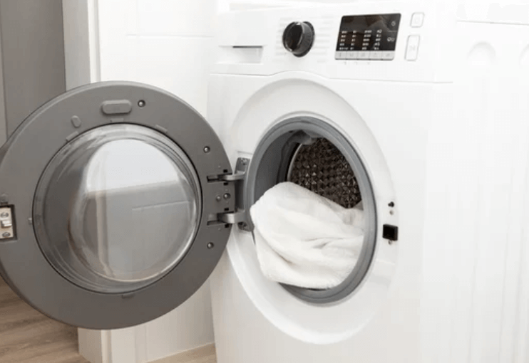 Primo piano sull'oblò di una lavatrice, da dove si possono intravedere degli asciugamani di color bianco
