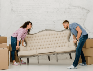 Una ragazza e un ragazzo che provano a sollevare un divano a 3 posti con una testiera alta e trapuntata