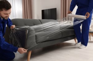 Due traslocatori che ricoprono un divano a tre posti con una pellicola protettiva