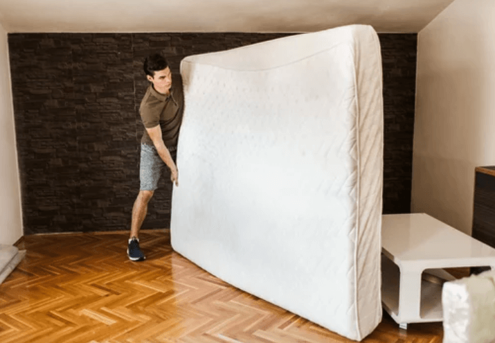 Un giovane ragazzo mentre sposta un materasso all'interno di una stanza vuota