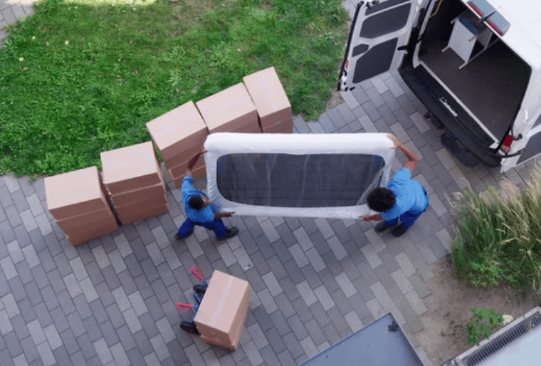 Due traslocatori, fotografati dall'alto, mentre spostano un materasso verso il furgone