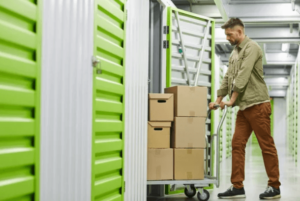Un uomo che con un carrello carico di scatoloni entra all'interno di un box individuale dalla serranda color verde